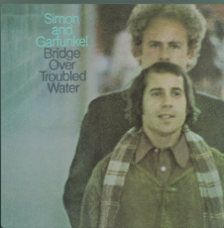 The album cover of the album Bridge Over Troubled Water by Simon & Garfunkel. Paul Simon is in the foreground and Art Garfunkel is standing behind him.